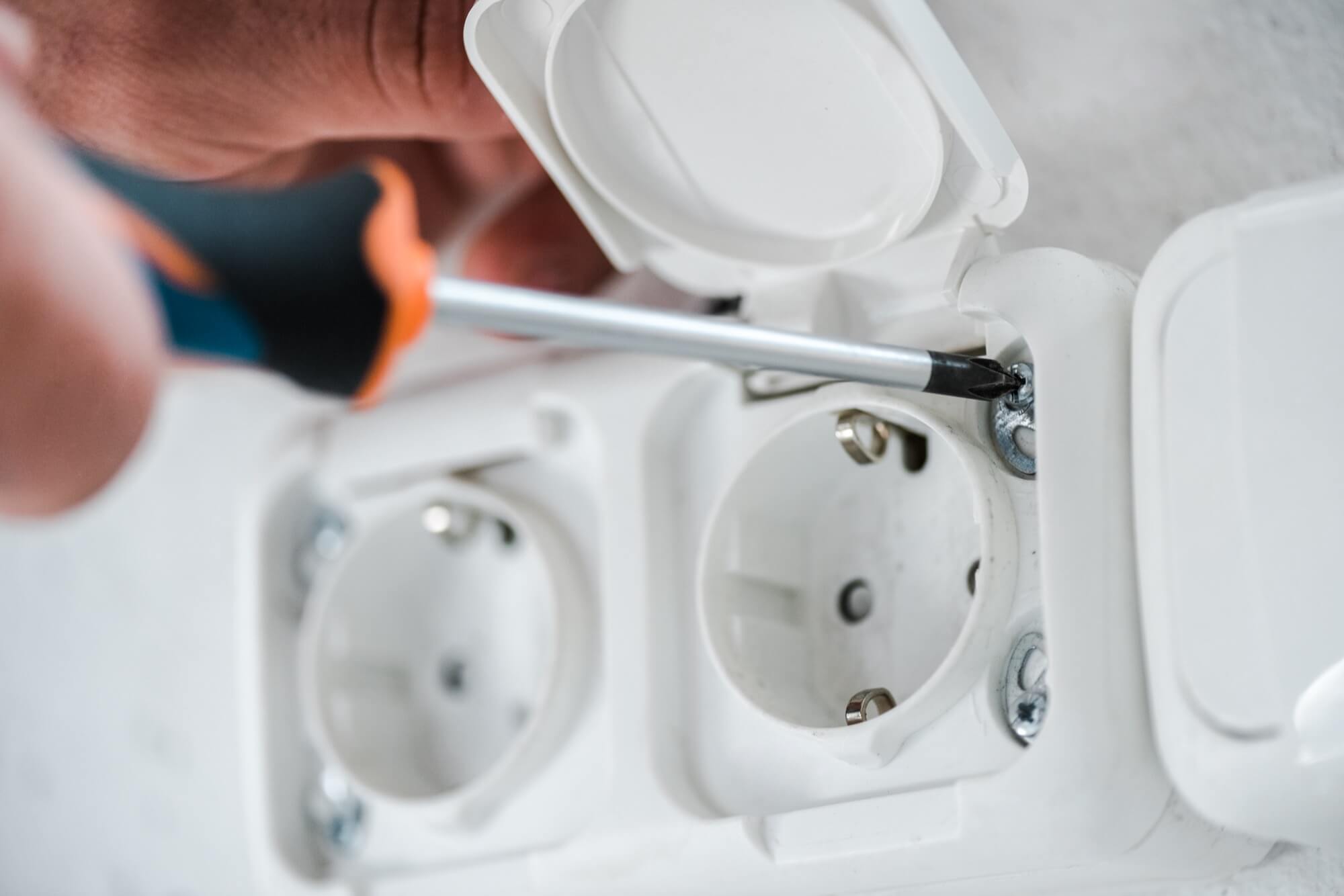Närbild av en elektriker som skruvar fast ett eluttag under installation.