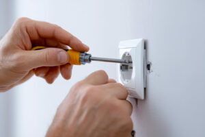 Närbild av en elektrikerhand som håller i en skruvmejsel vid installation av ett vägguttag. Belyser vikten av professionell installation och korrekta verktyg.
